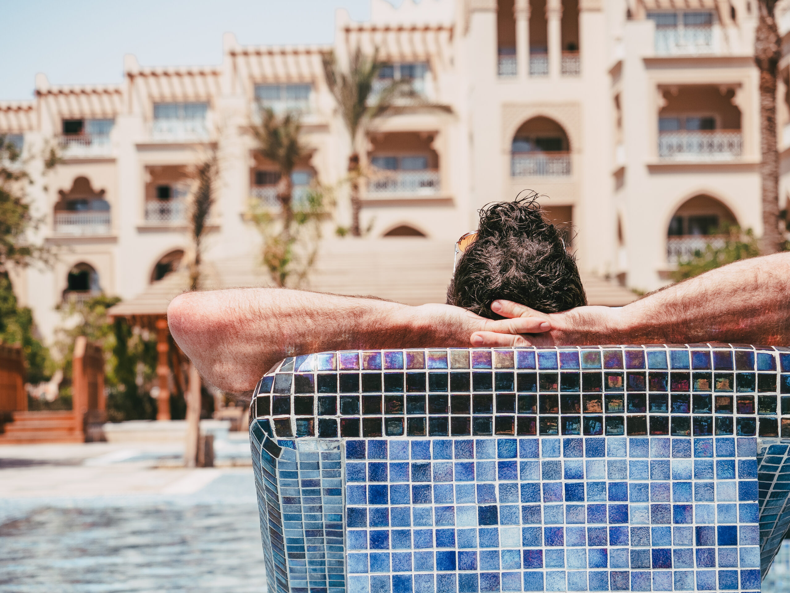 Attractive man lying in a sun lounger on the background of the swim pool. Back view, close-up, outdoors. Vacation and travel concept